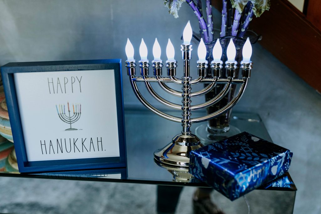 Modern menorah with framed Hanukkah greeting and gift on a glass table.
